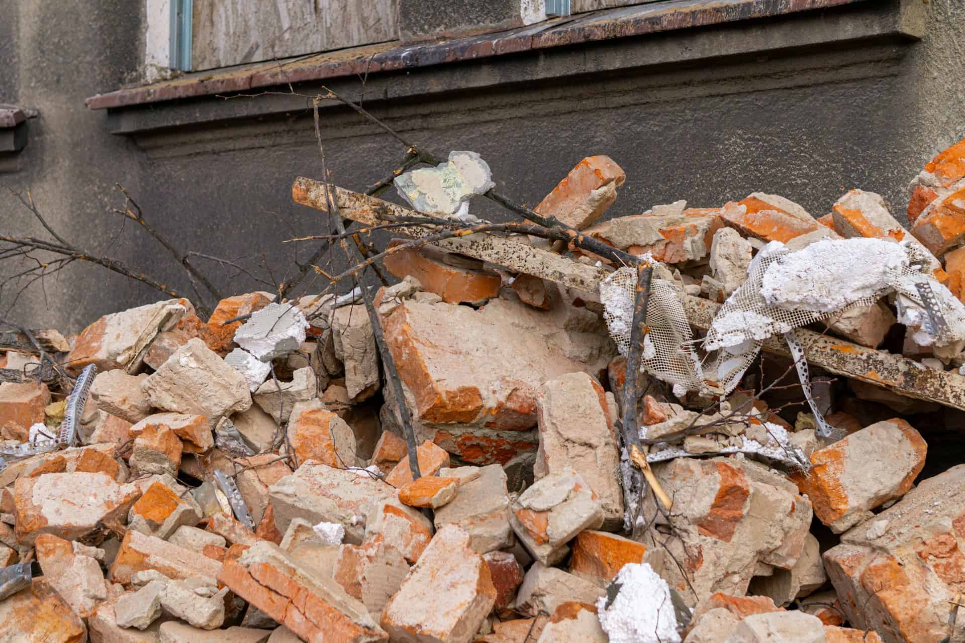 Construction waste from a renovation, mostly composed of bricks and mortar, piled up under a window sill.