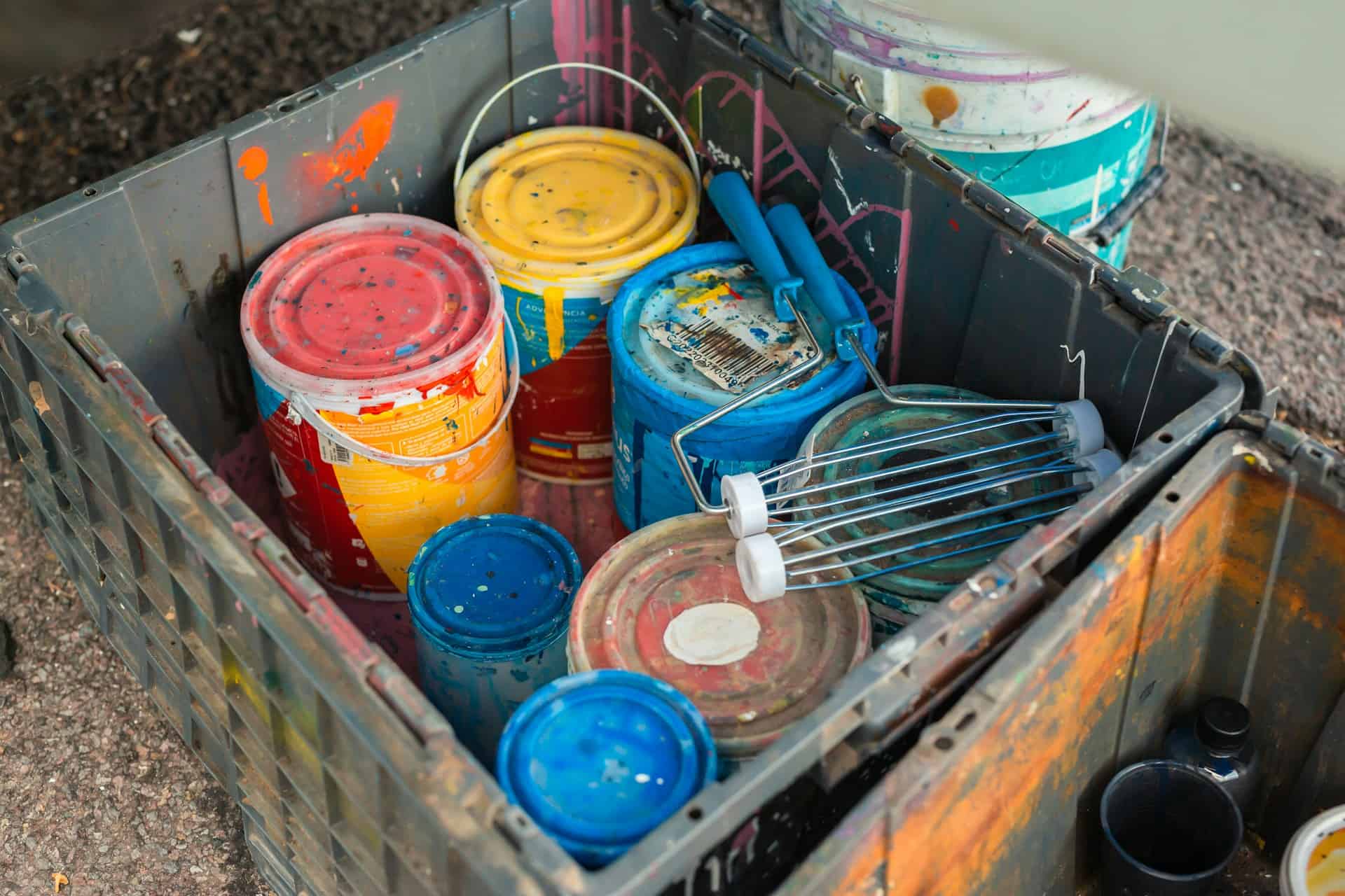 Plastic crate holding 7 cans of old paint and two rollers. 